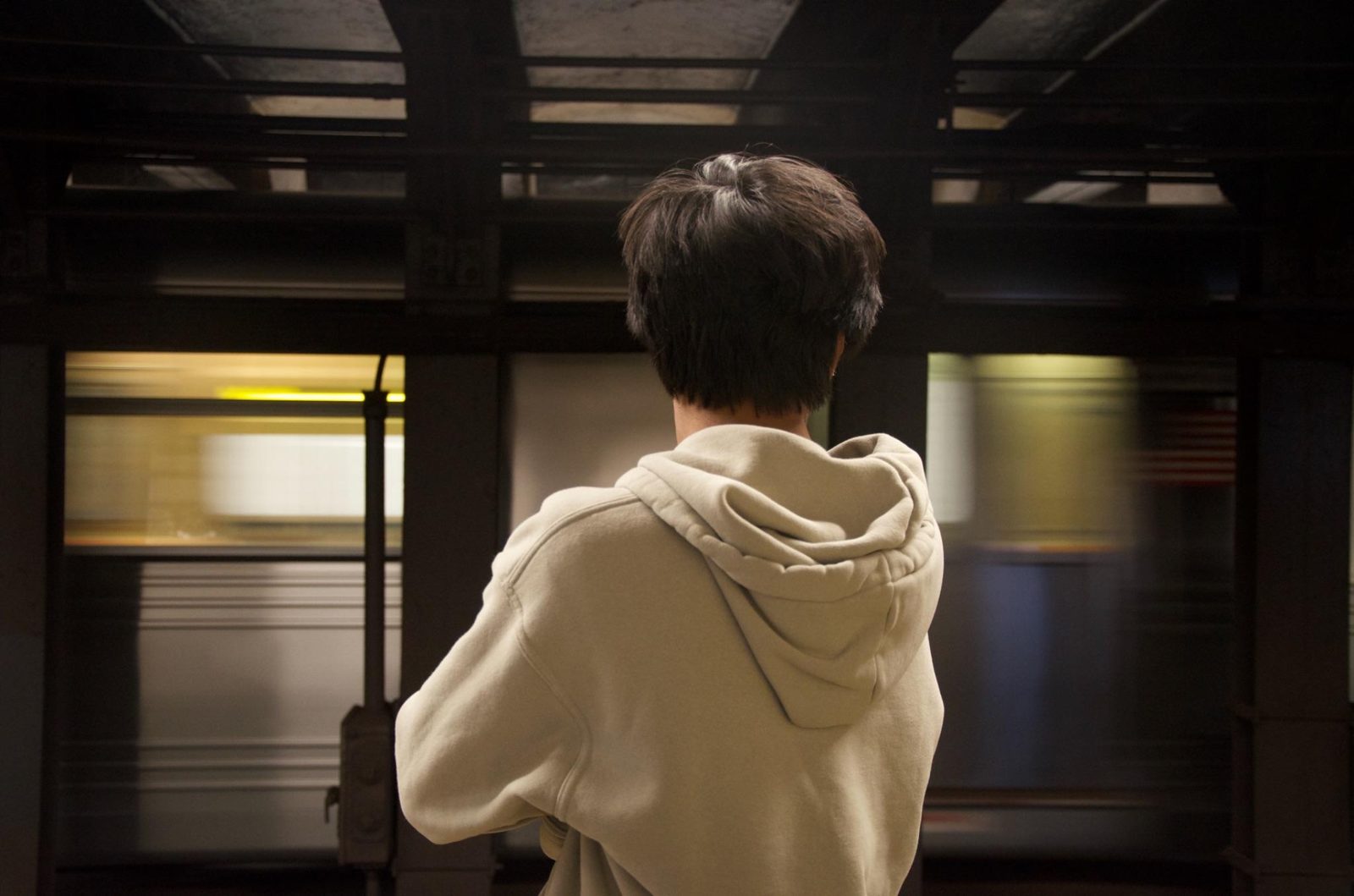 A person in a hoodie watches a subway train blur past